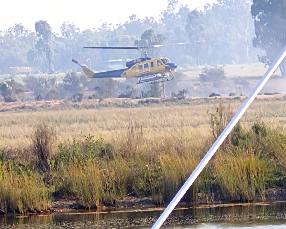 A helicopter leaves with a load of water from a farm dam on the property where Norm Sutton lives. Harnessing the use of local resources.